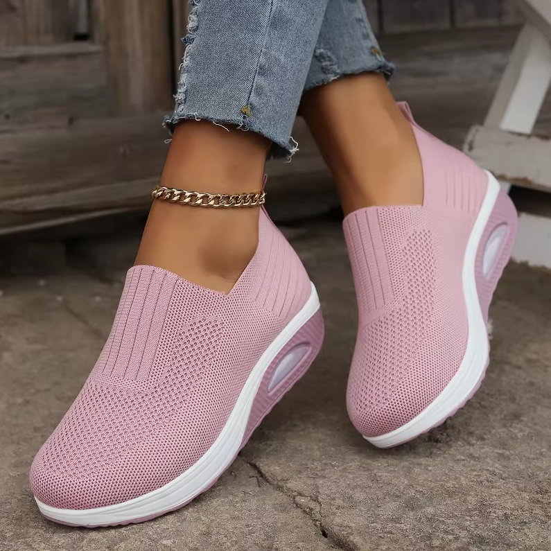 A pair of pink air cushion shoes with a mesh upper and a white sole, worn by a person with jeans.