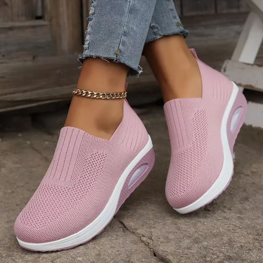 A pair of pink air cushion shoes with a mesh upper and a white sole, worn by a person with jeans.