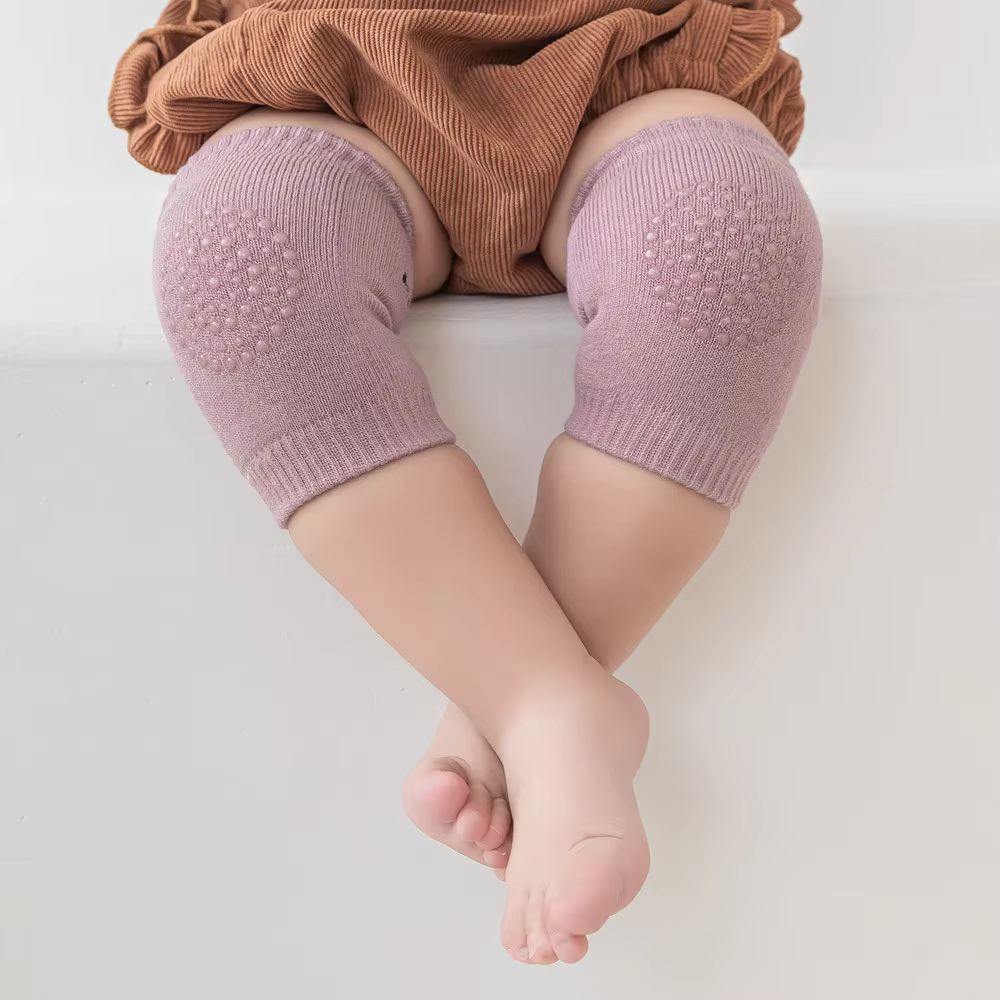 Kids knee sleeve worn on both knees of a baby in a pink color, showing padded grip panels during seated play.